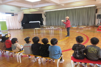 写真：学芸員になって説明する先生の話を聞いている年中さん