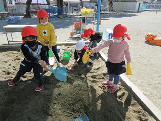 写真：砂場で大きなスコップを使ってお山を作る子ども達