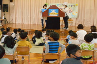 大型紙芝居を演じる教師とみている園児