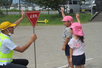 「止まれ」の標識を見て手を挙げて道路渡る園児たち