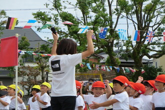 ごほうびのメダルを見せる職員とそれを見て喜ぶ年少組の子ども達