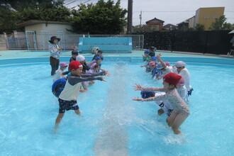 プールで水をかけあう年長児