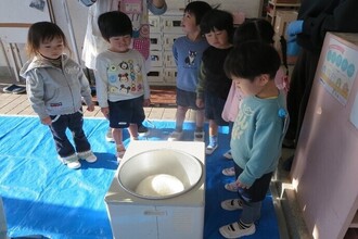 写真：餅つきの機械を覗いている年少児