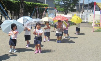もも組さん、傘を差して園庭を歩いています