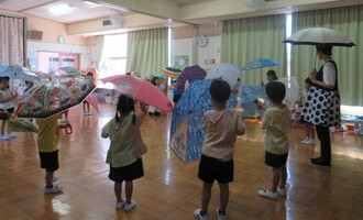 き組とみどり組、園長先生の話を聞いて一緒に傘を差す練習をしています
