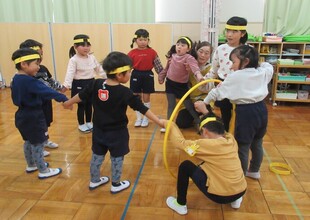 チームのみんなで手をつないで円になってフラフープをくぐっています
